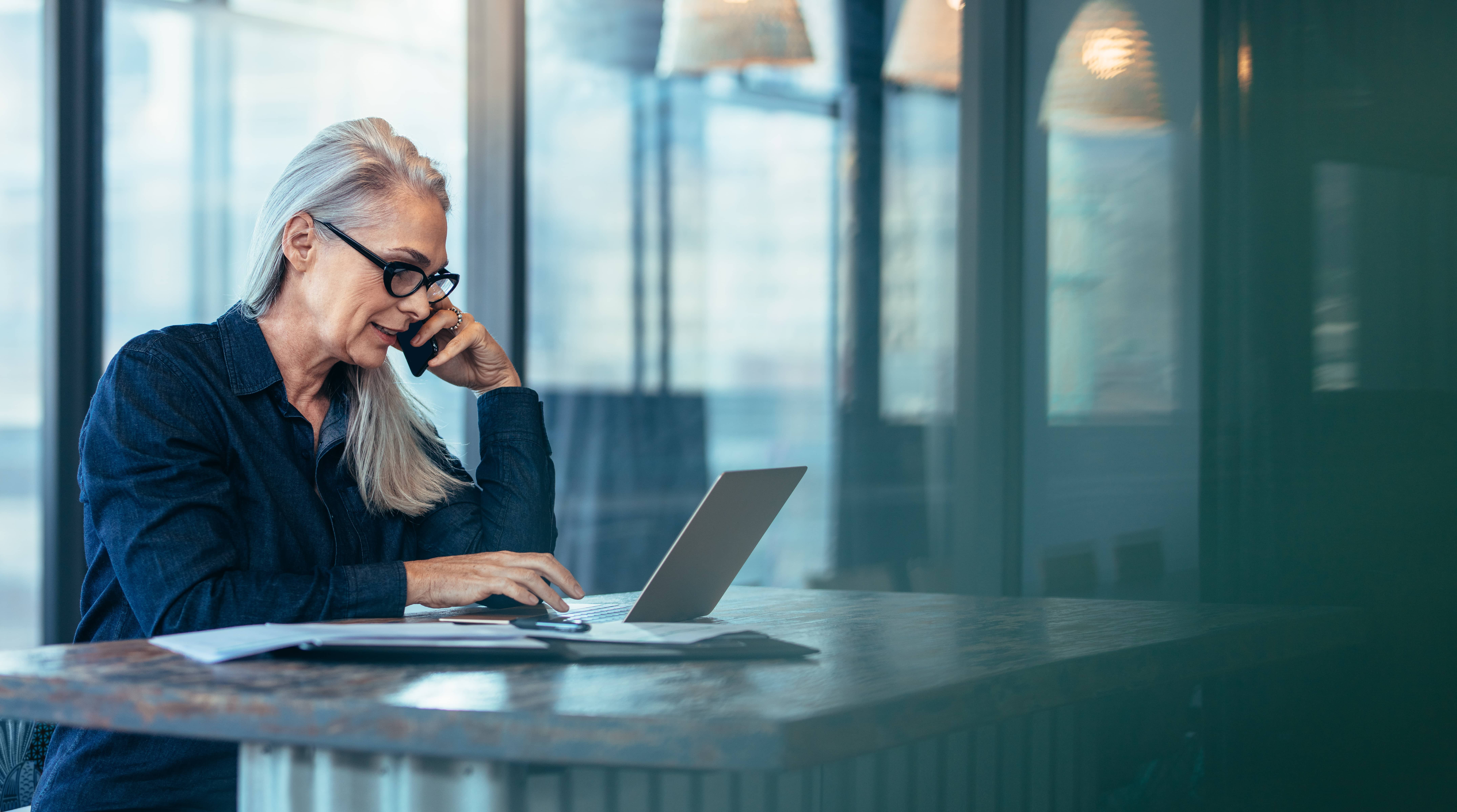 Woman with long hair talking on cell phone looking at computer