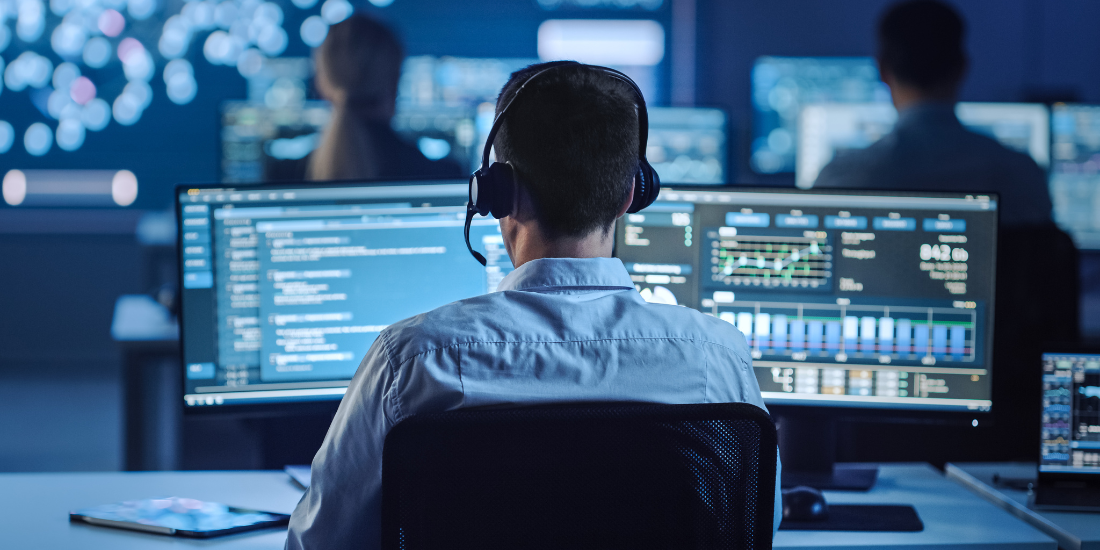 The back of a contact center worker sitting in front of computer monitors with charts on the screens.