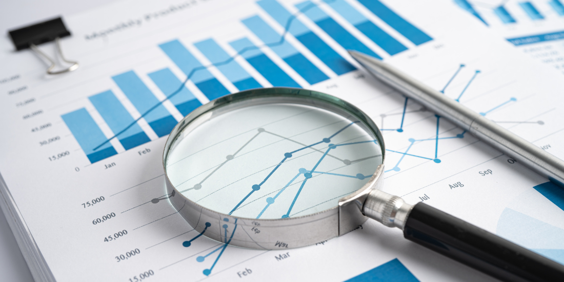 A magnifying glass rests on a paper showing bar graphs and scatter plots and data points. 