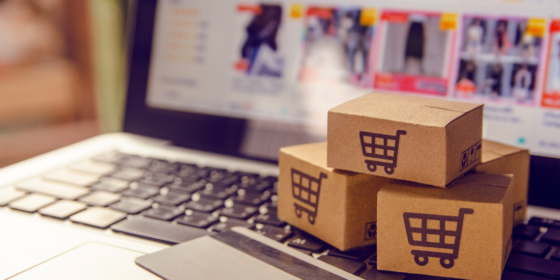 Cardboard packages with shopping cart icons stacked on a laptop displaying an online shopping website.