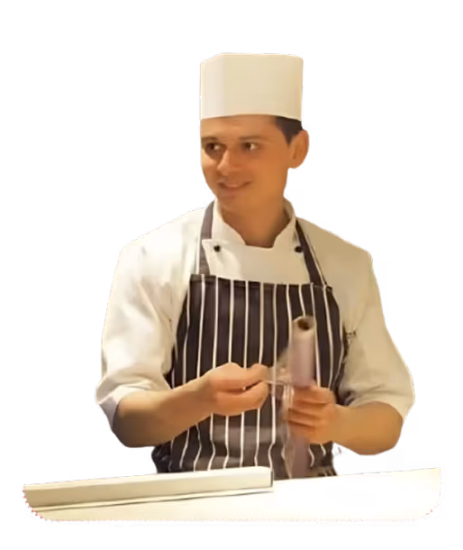 Bucătar într-un șorț cu dungi și șapcă albă, ținând un obiect cilindric în mâini.