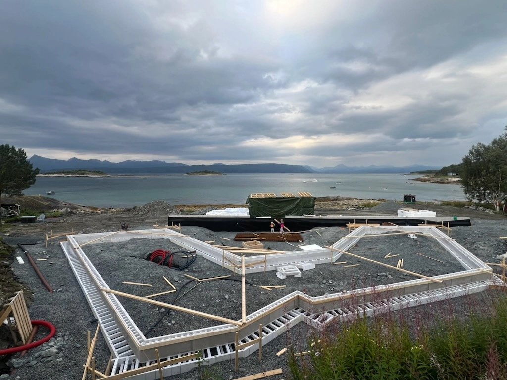 Byggeplass med støpt grunnmur og isolerte forskalingsblokker på en tomt ved sjøen