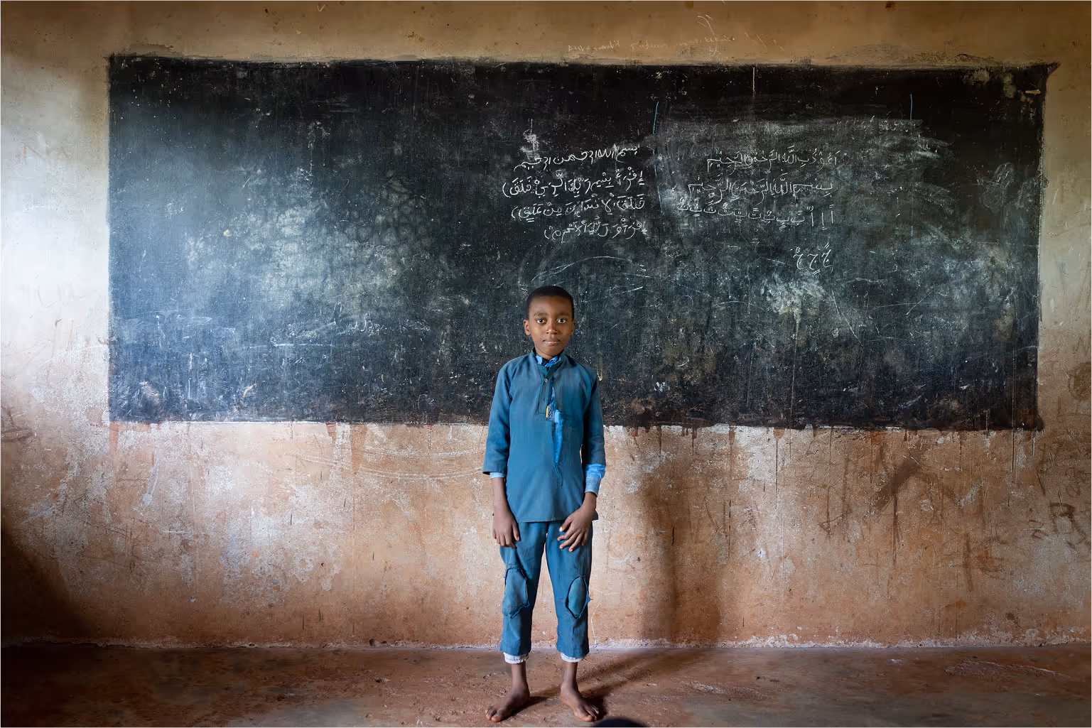 Cute African boy standing in front of messy blackboard smilling