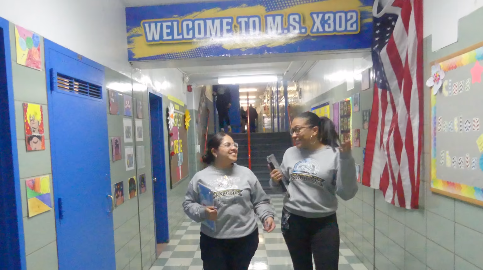 Two students walking and smiling in MS X302 school hallway