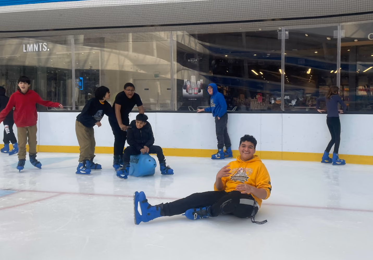 Students laughing and ice skating together at an indoor rink
