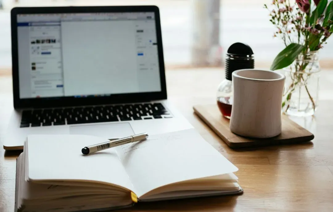 Laptop on desk with notebook.