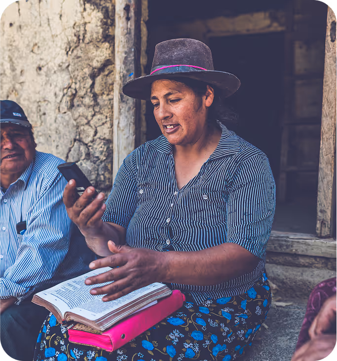 A south American woman sitting in front of a wooden window holding a phone. 