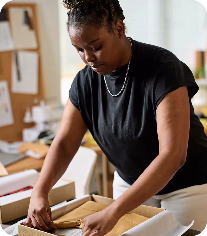 Mulher embalando um produto em uma caixa de papelão em um ambiente interno.