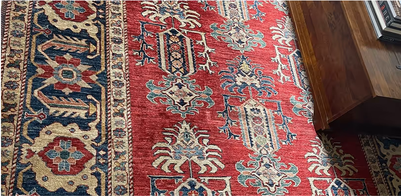 Intricately patterned red and blue oriental rug next to a wooden table with books.