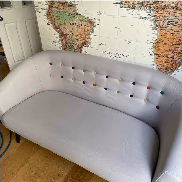 Light grey couch with multicoloured buttons on the backrest placed in front of a wall map showing South America and Africa.