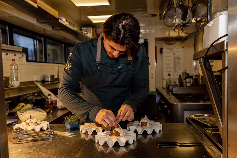 Chef bereidt zorgvuldig gerechten op een roestvrijstalen werkblad in een professionele keuken.