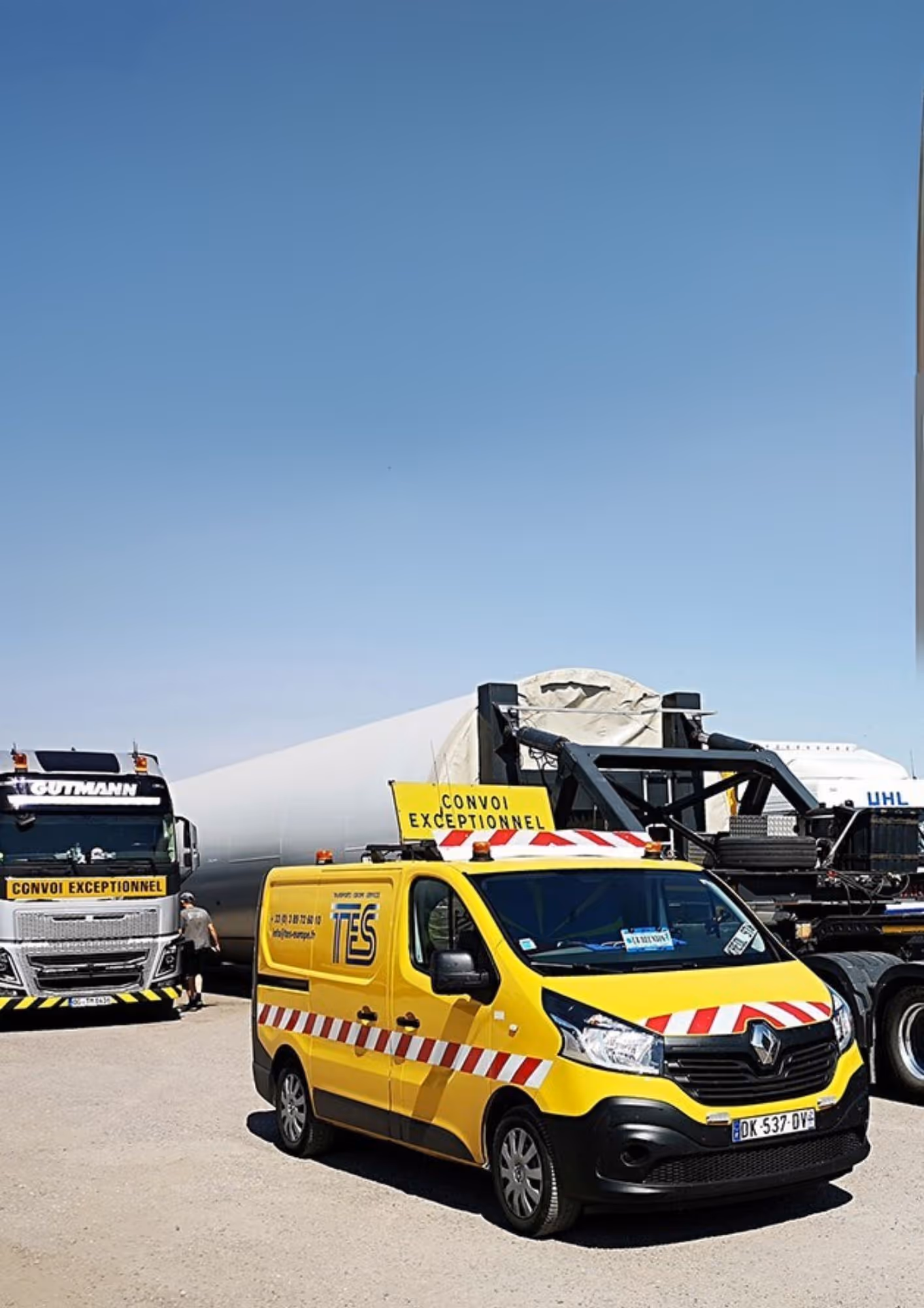 Vehicul galben de escortă cu semnul „Convoi exceptionnel” în fața unui camion mare care transportă o componentă uriașă pe un transport special.