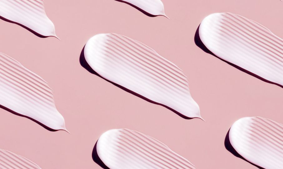 Photo of dashes of white cream on a pink surface