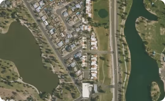 Aerial view of a landscape showing a dense residential area on one side, separated by a major road from a large lake on the other.