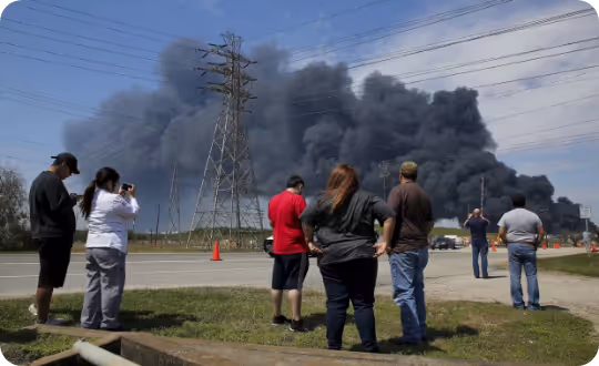 Seven figures stand observing a scene where a plume of gray smoke rises next to an electrical pylon.