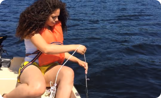 A researcher in full safety gear sits in a small boat, operating specialized equipment to monitor water quality on a lake or river.