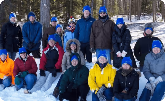 A group of 17 researchers dressed for cold weather posed in a snowy forest.