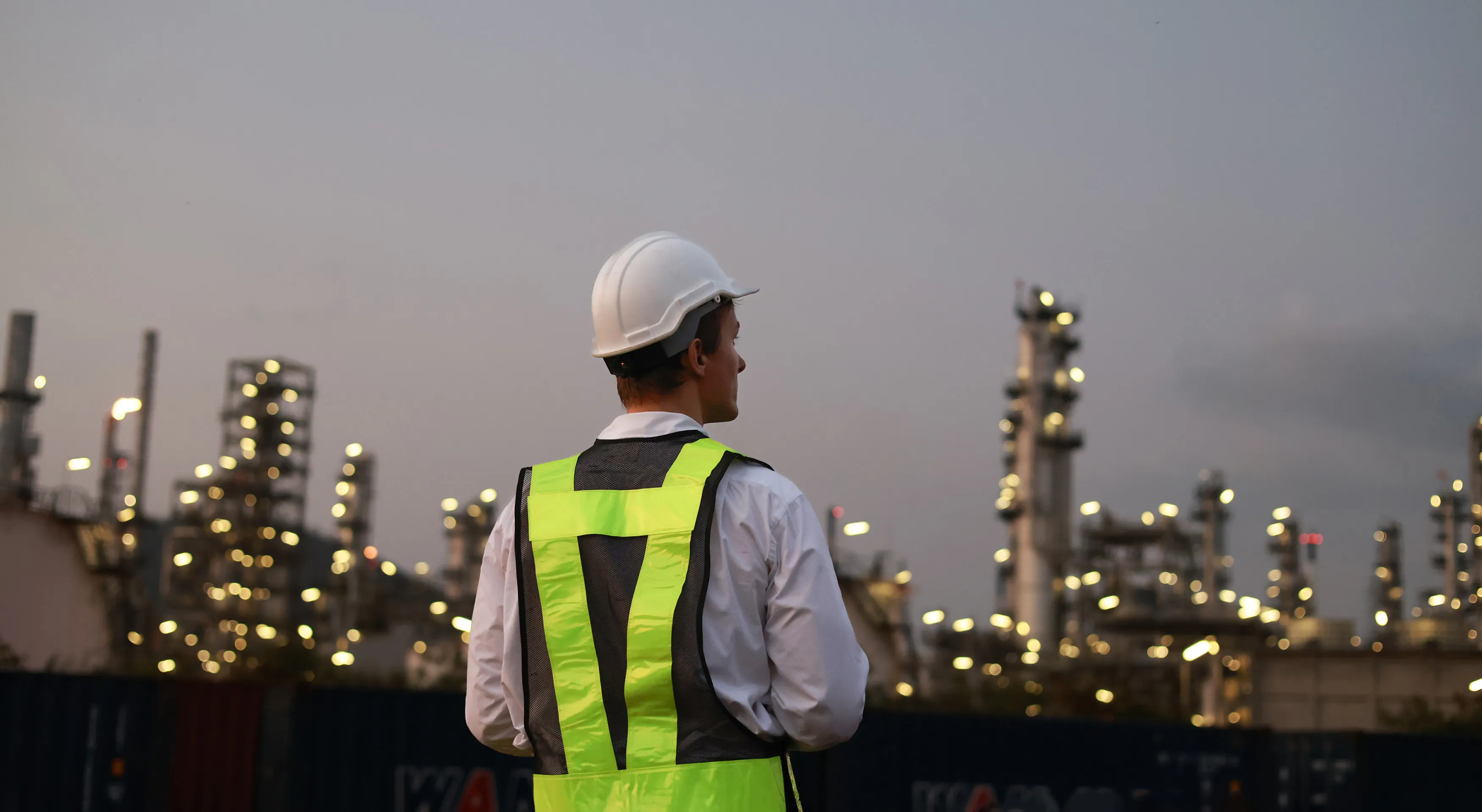 Engineer in hard hat and hi-vis vest overlooking an industrial refinery at dusk