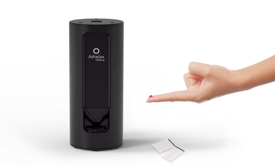Black Athelas Home testing device next to a hand with a drop of blood on the fingertip and two test strips on a surface.