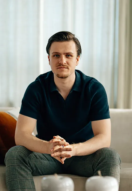 A man with a beard and blue shirt sitting on a couch.