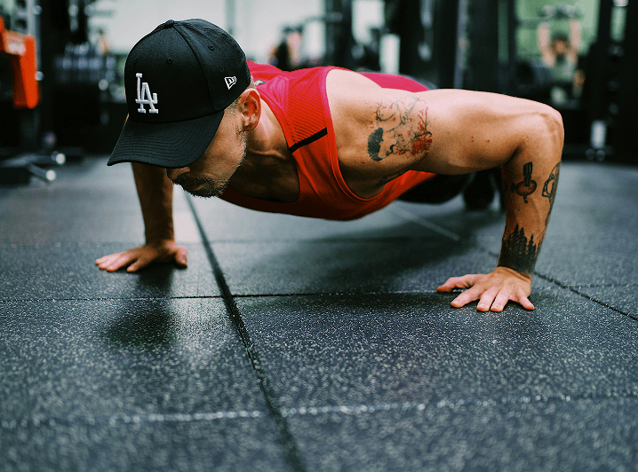 A man with a baseball cap doing a pushup in a gym