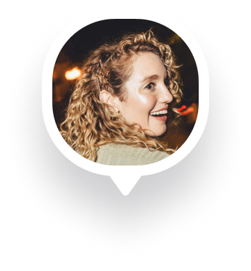 Smiling woman with curly blonde hair looking to the side in a nighttime setting.