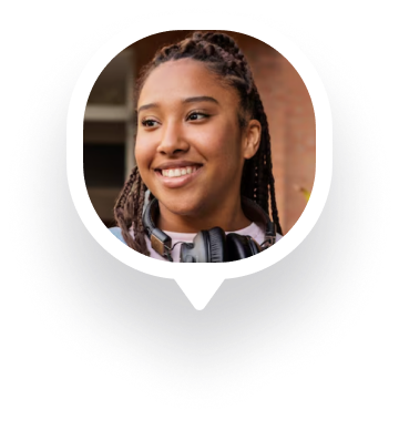 Smiling young woman with braided hair wearing headphones around her neck in an outdoor setting.