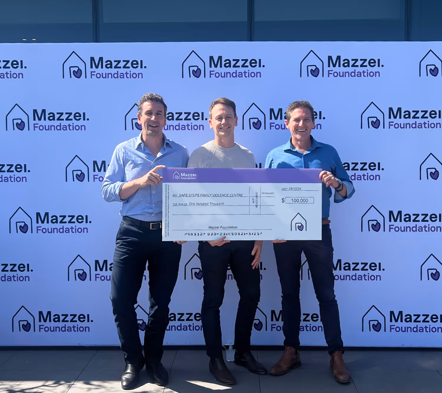 A group of three men standing next to each other holding a cheque