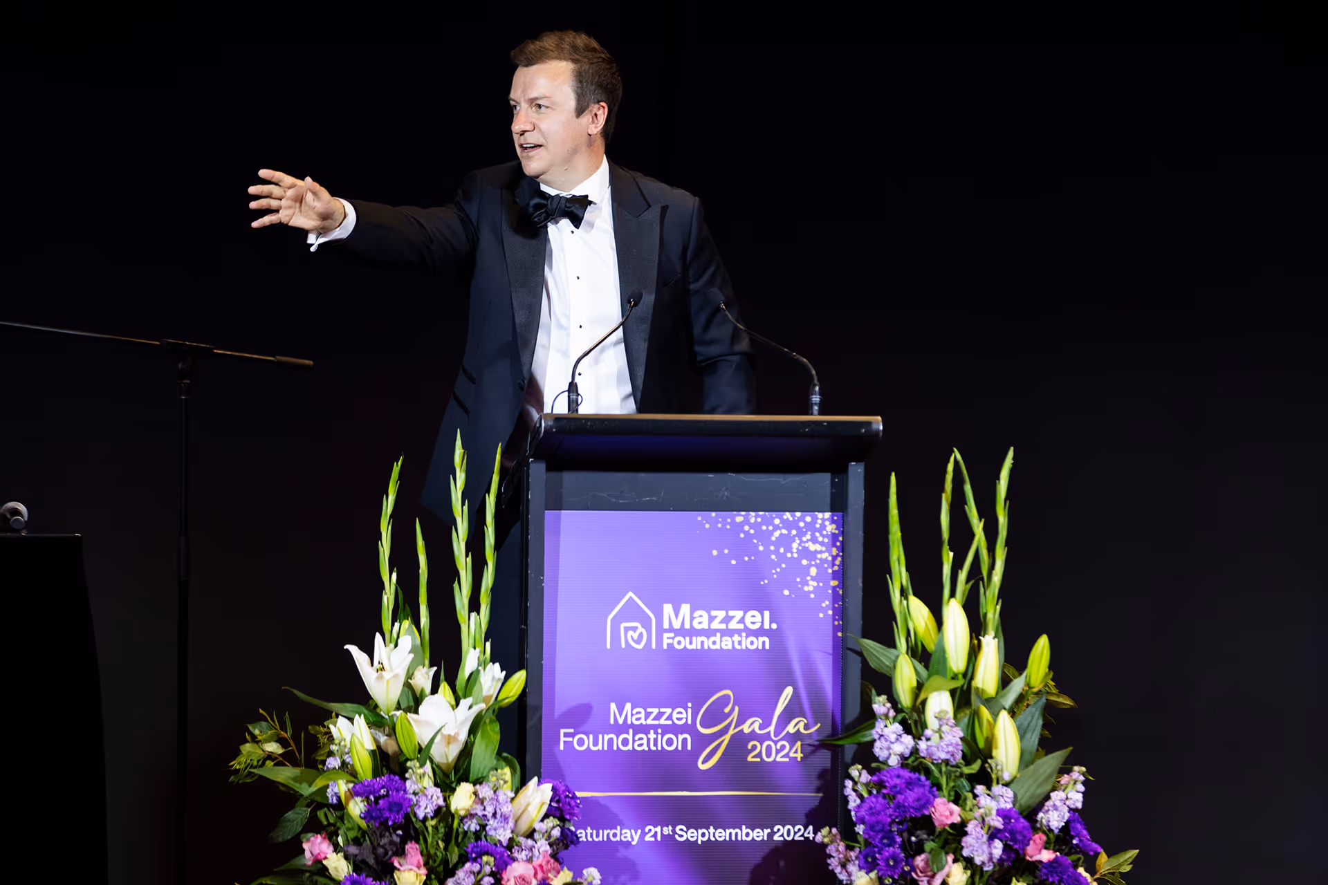 A man in a tuxedo speaking at a podium.