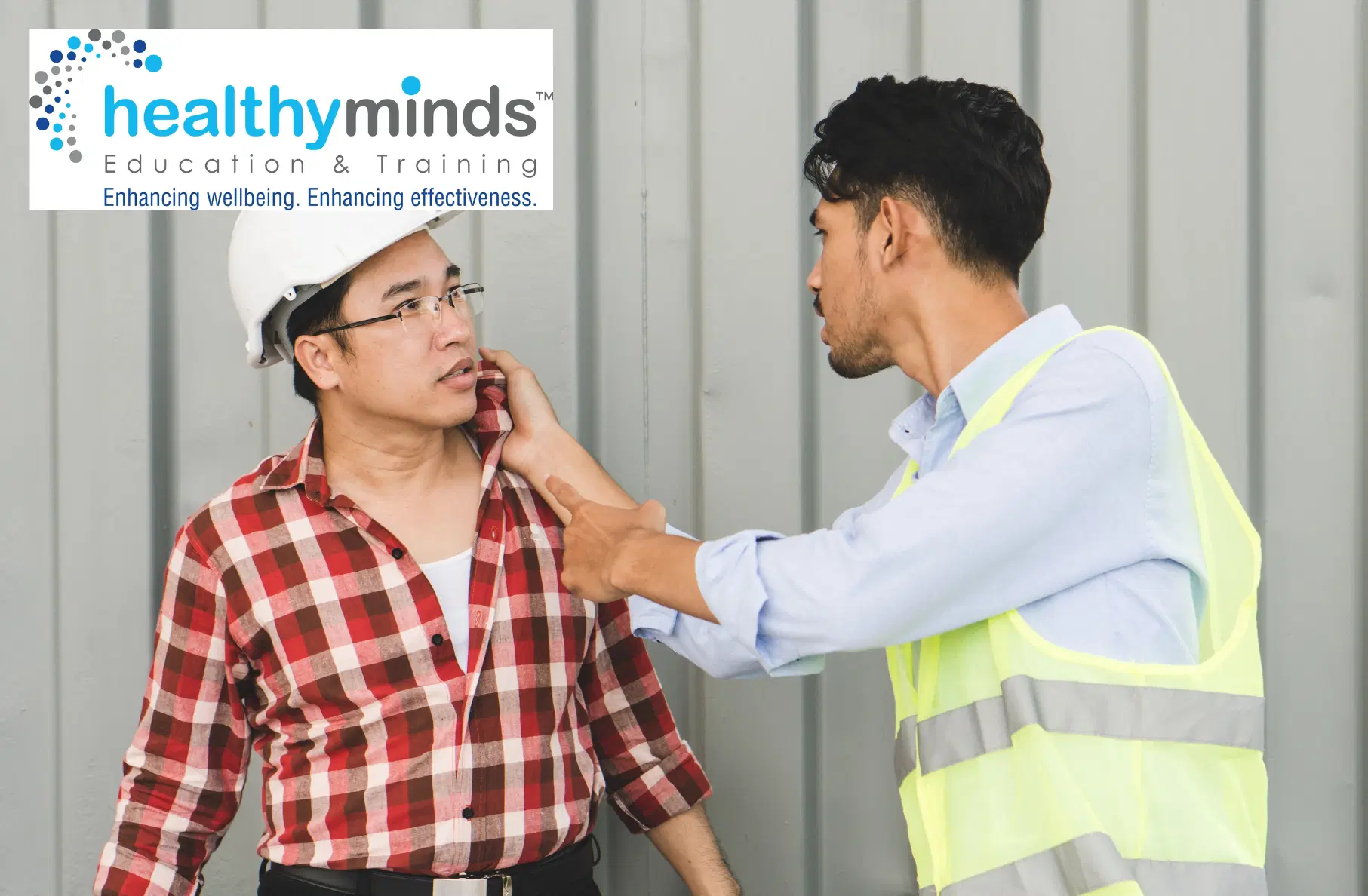 Construction worker in yellow safety vest grabbing the collar of another worker wearing a white hard hat and red plaid shirt in a confrontational manner.