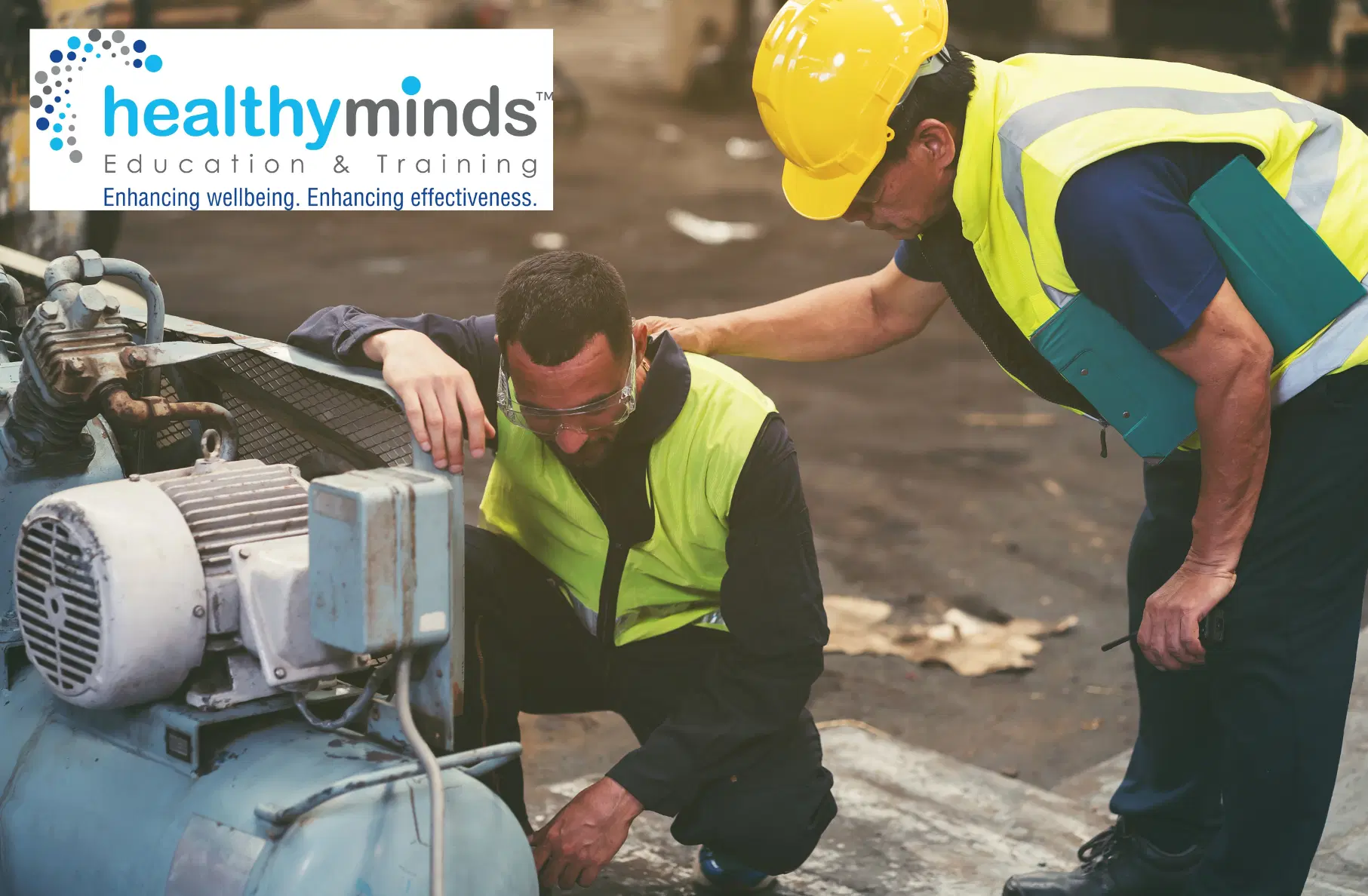 Two industrial workers in safety vests inspecting machinery in a factory, with one worker comforting the other by placing a hand on his shoulder.