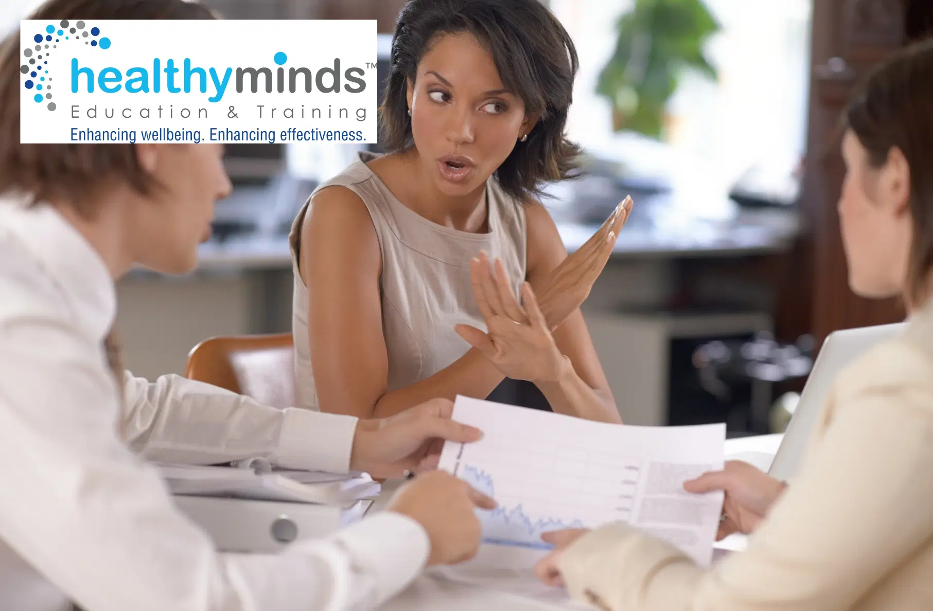 Woman making a stop gesture with her hands while two colleagues discuss a document with graphs at a meeting.