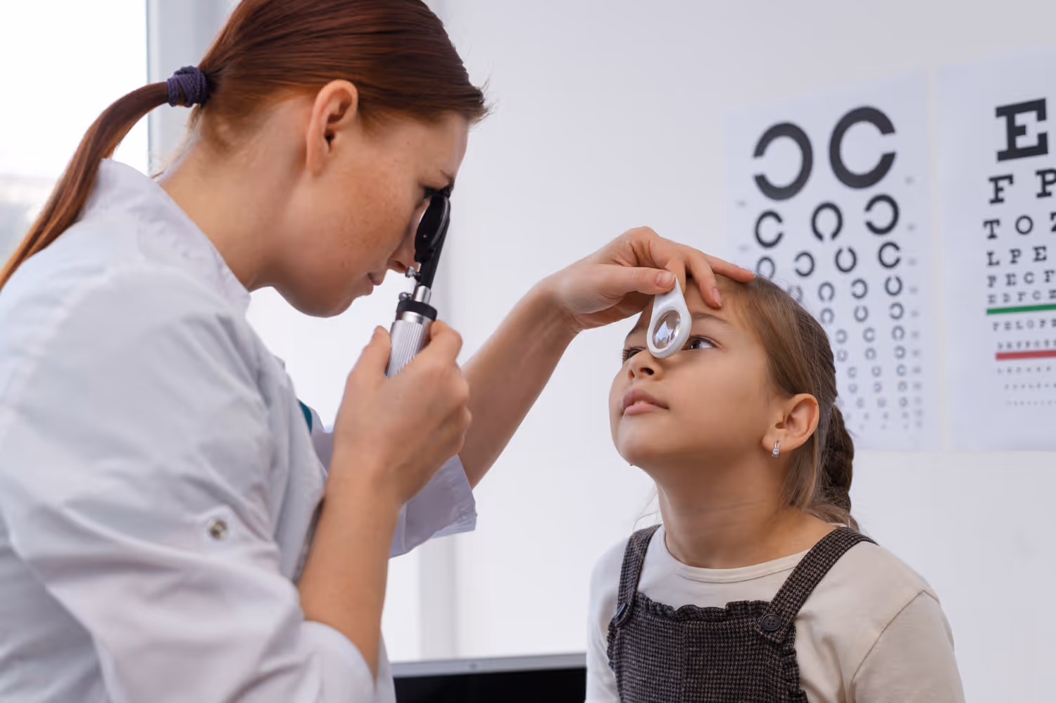 Eye doctor examining young patient's vision with eye chart in background