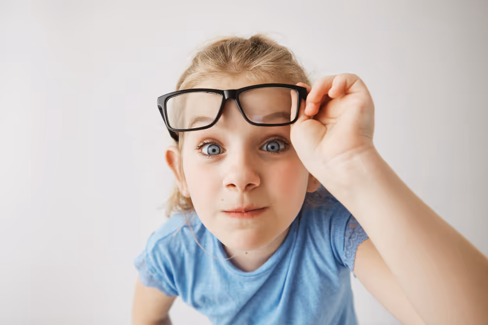 Child in oversized glasses lifting frames, looking curious and playful