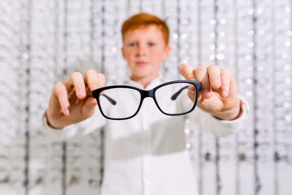 Child holding black-framed glasses in front of blurry background
