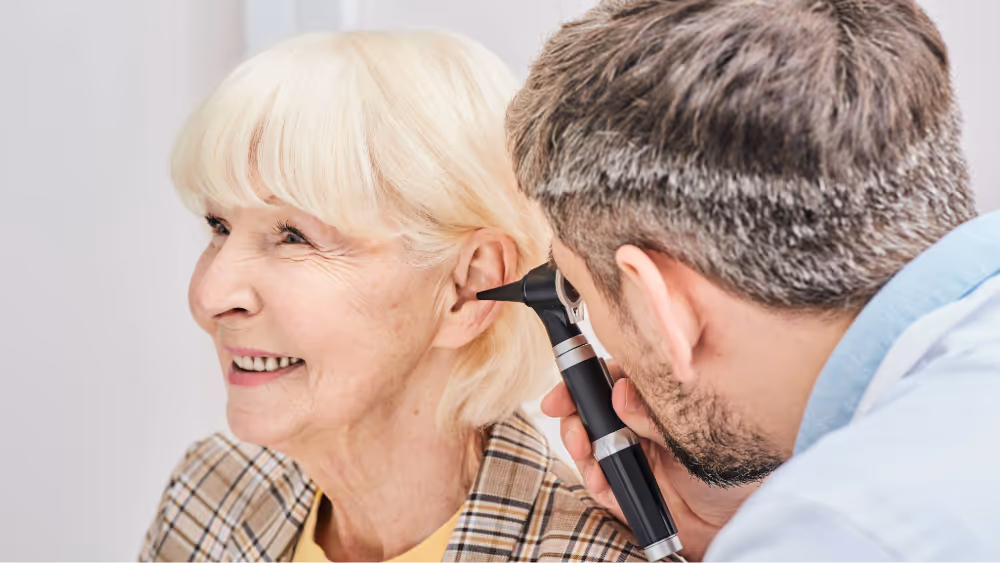 Audiologist examining older patient's ear with otoscope during eye check-up