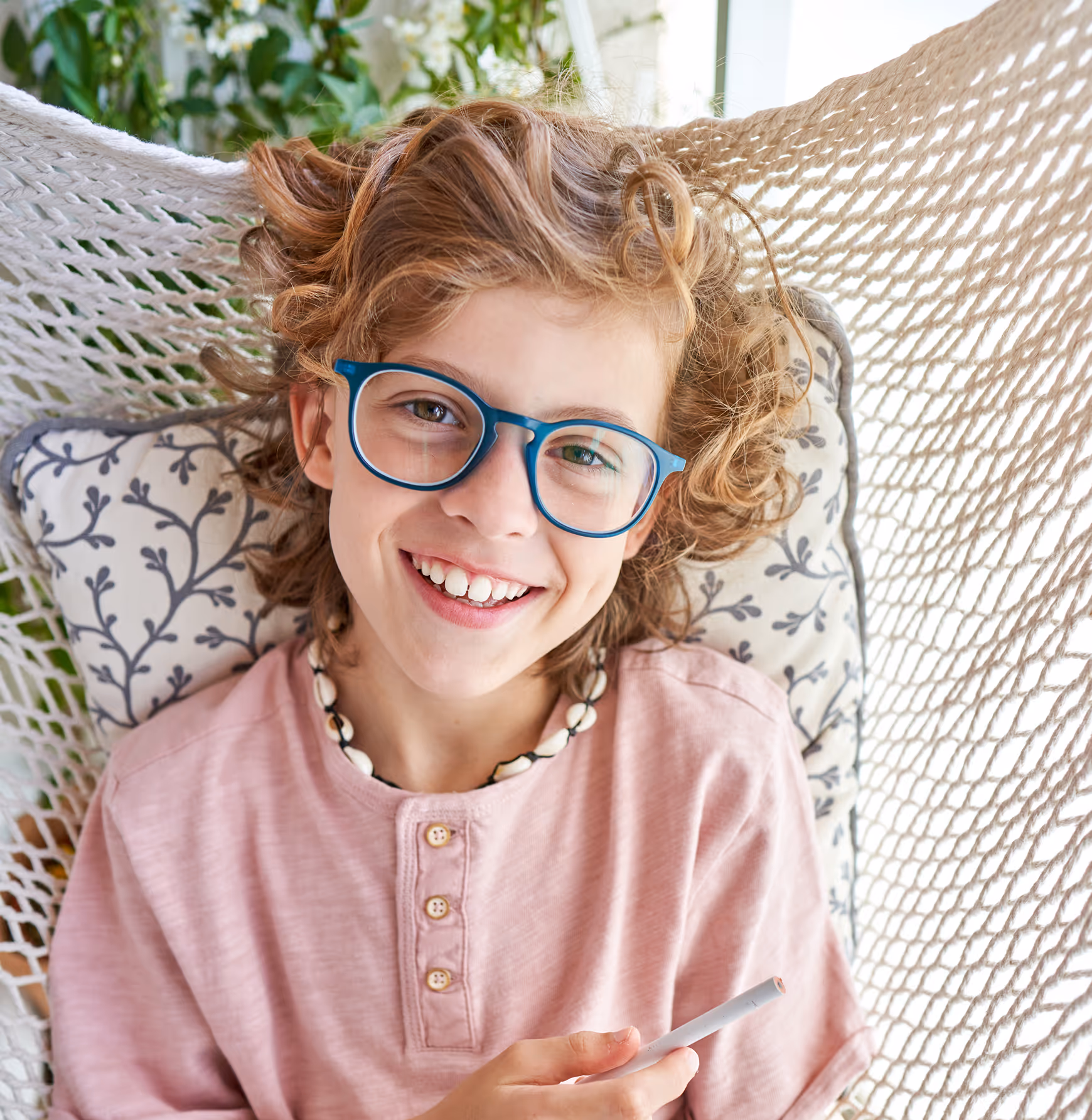 Smiling child with curly hair and blue glasses sitting in woven chair