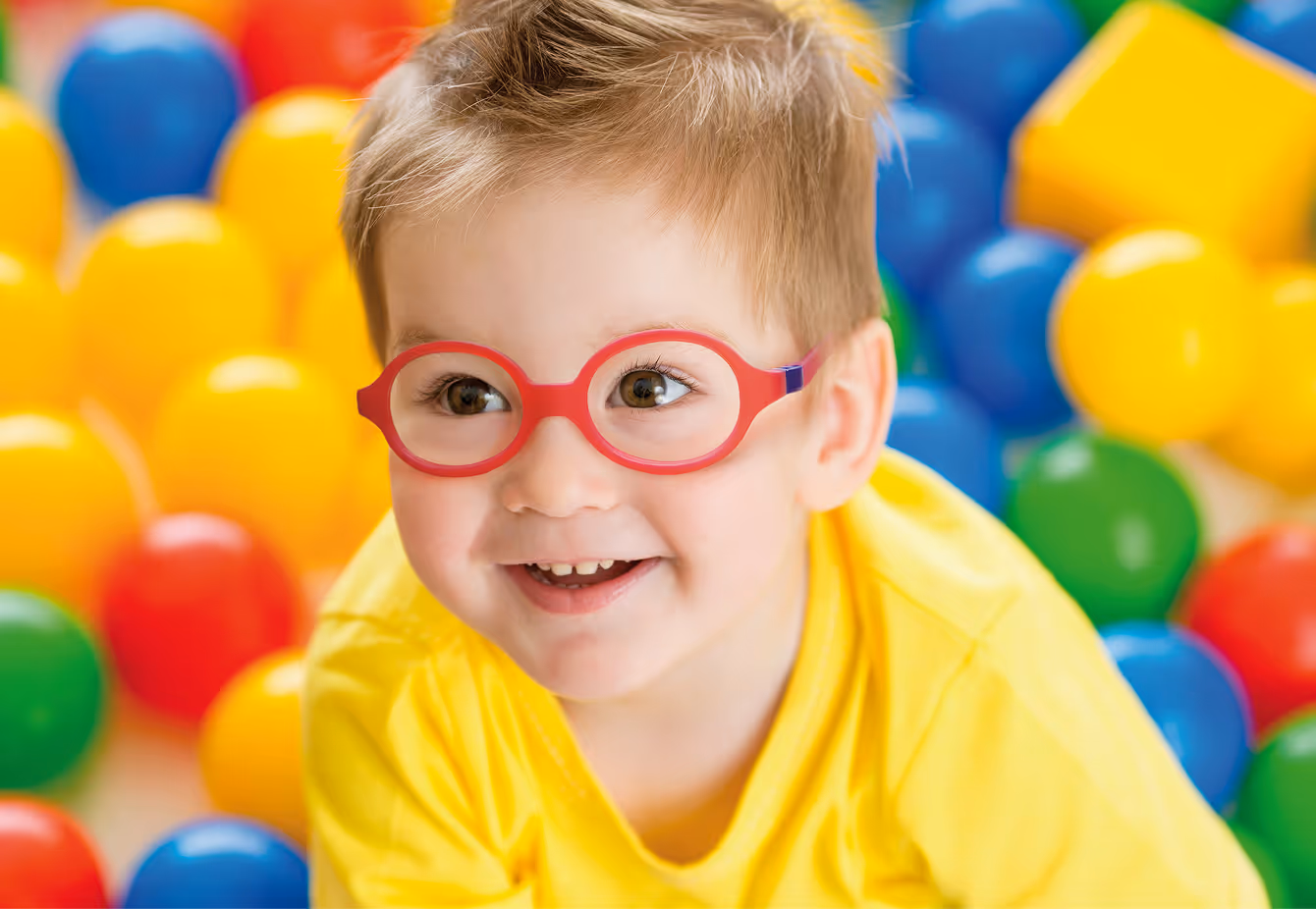 Smiling child in red glasses surrounded by colorful balls