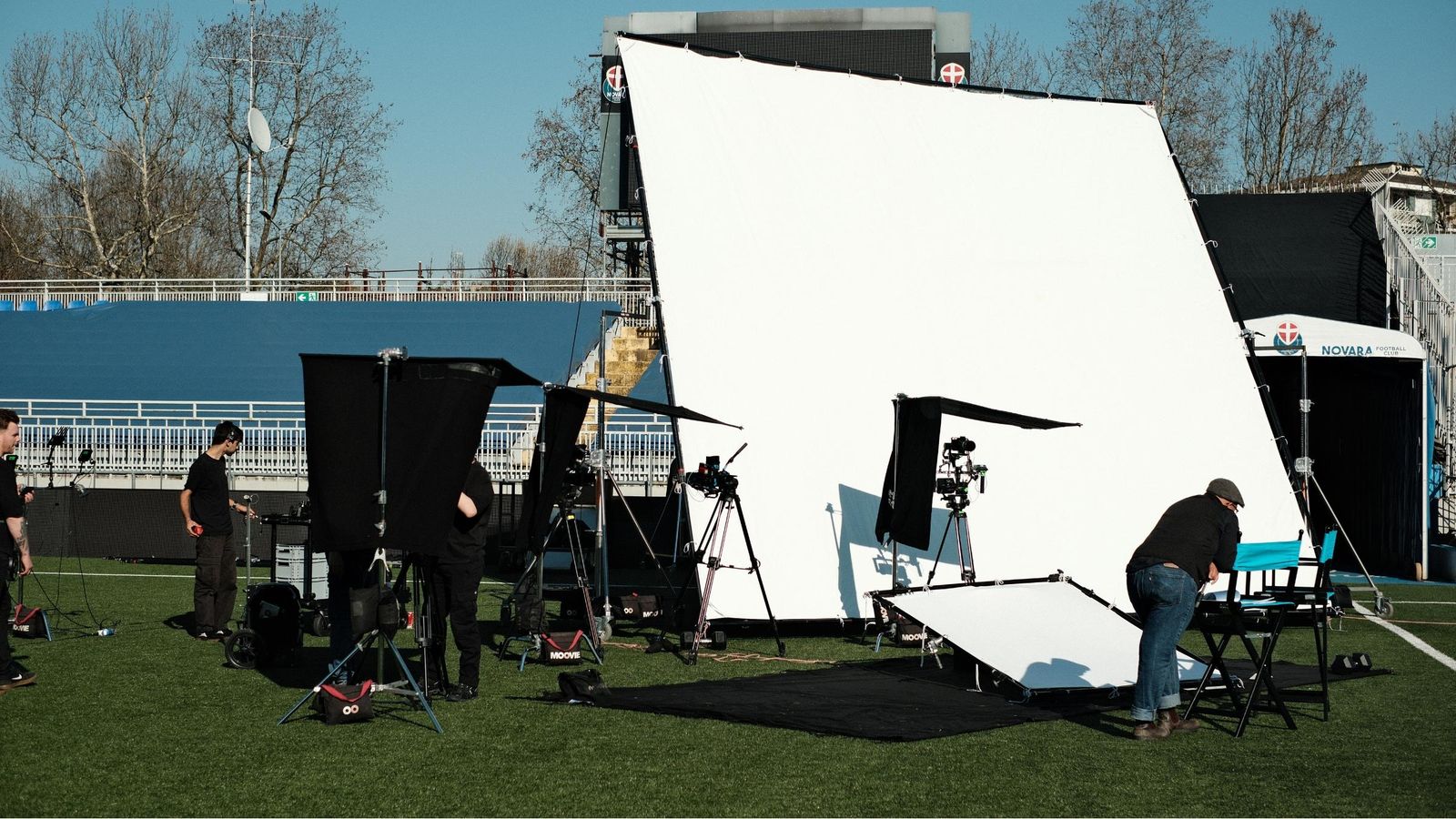 Crew setting up lights and a large white frame on the pitch at the stadium in Novara