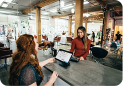 A woman at a salon reception desk interacting with a receptionist using a tablet.