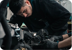 Mechanic wearing gloves working on a car engine with focused expression.