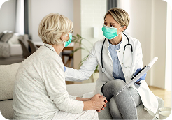 Female doctor wearing a face mask consulting with an elderly female patient in a living room.