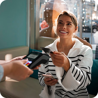 Smiling woman using a credit card to make a payment on a card reader at a cafe.