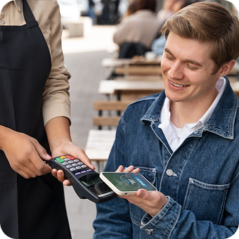 Man smiling and making a contactless payment with his smartphone to a cashier holding a card reader.