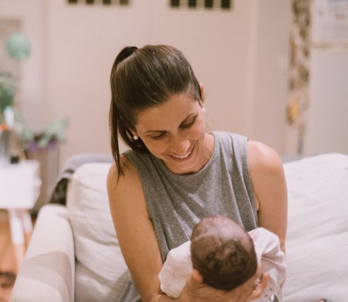 A smiling mother holding her newborn baby in a warm home environment, showing love and early connection.