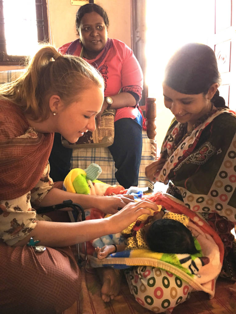 A volunteer gently checking on a newborn while visiting a mother and family at home after birth.