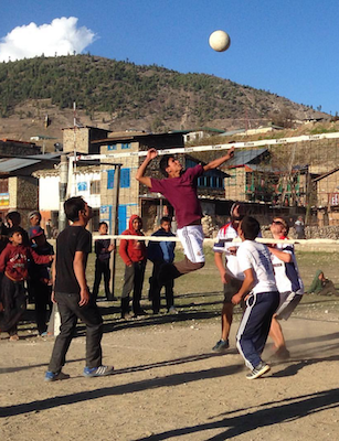 Young men play an energetic volleyball game in a mountain village surrounded by local onlookers.