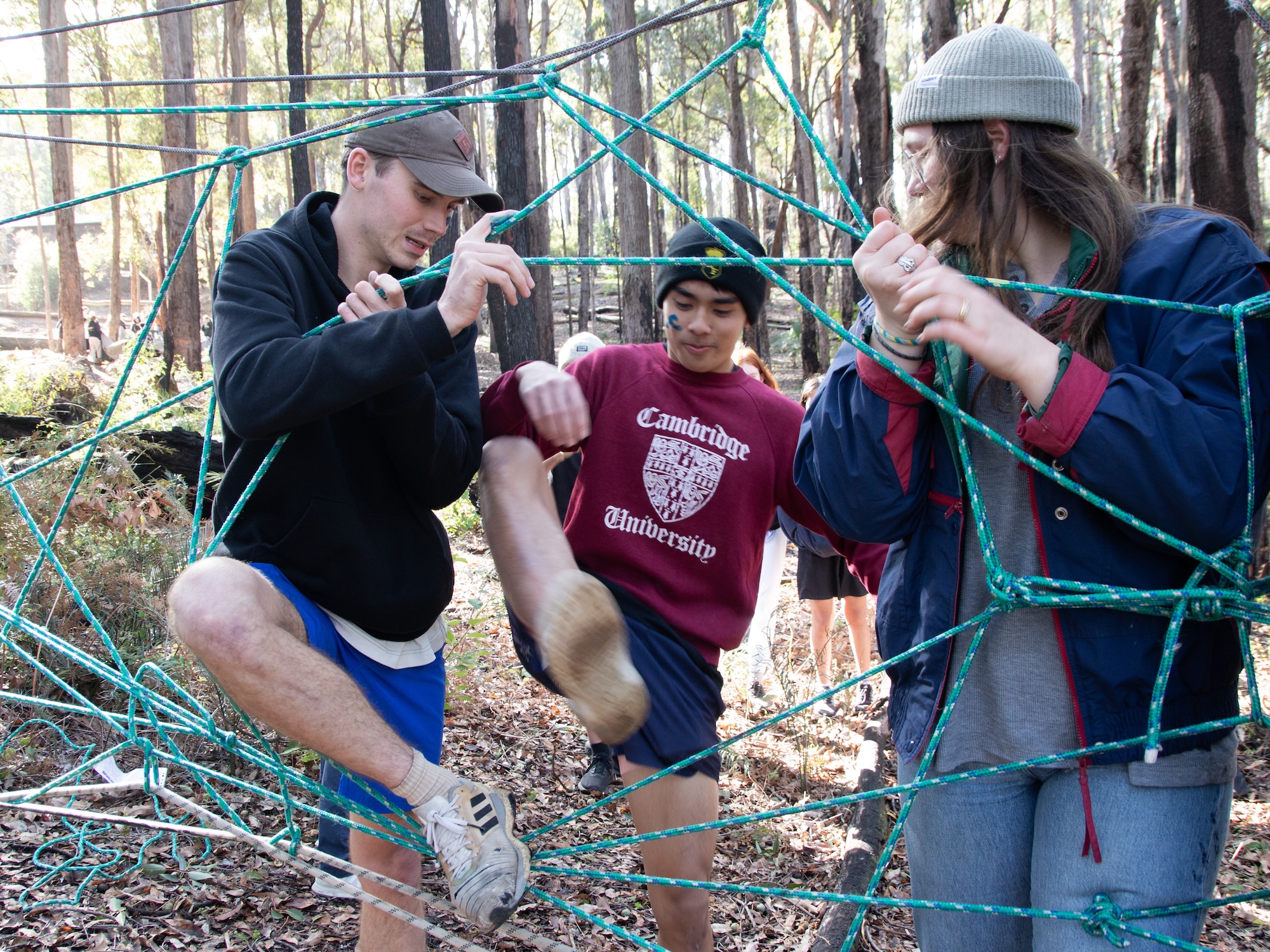 Young people working together to navigate a rope web challenge in the forest during Winter Camp team activities.