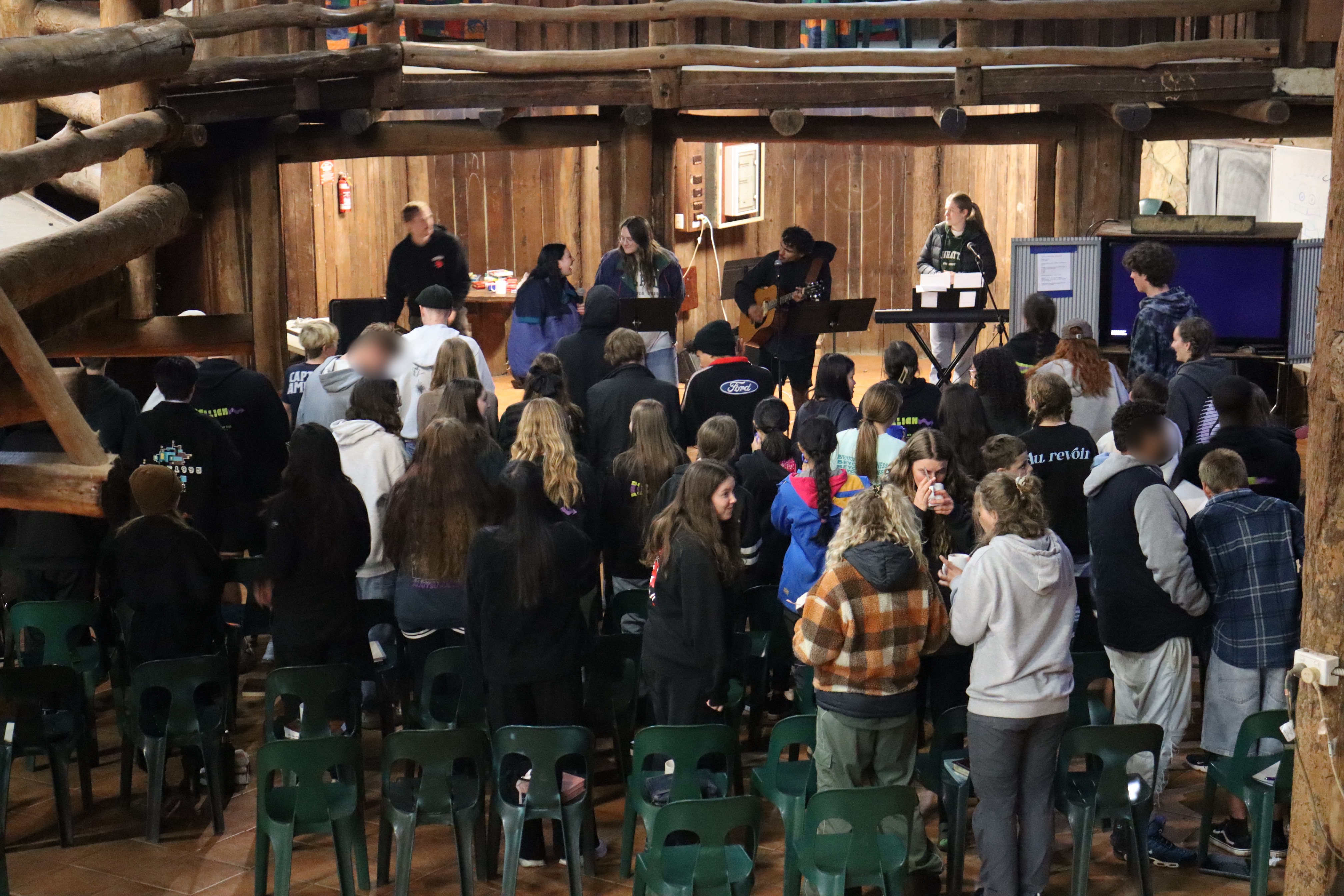 Group of youth gathered indoors in a wooden lodge for worship, singing, and fellowship during Winter Camp.