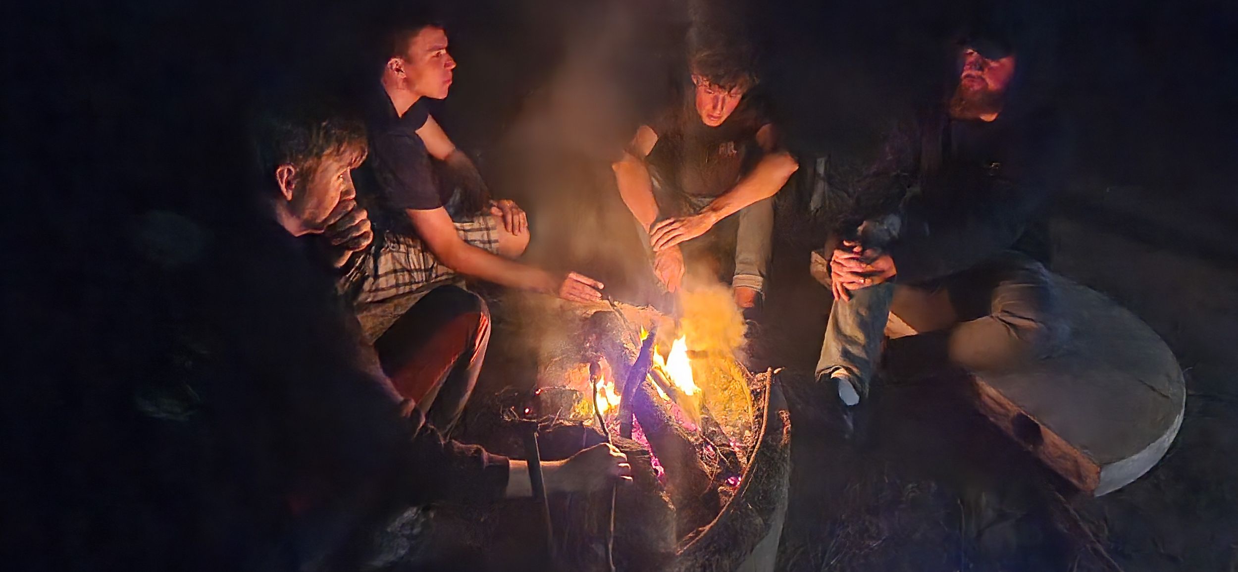 a group of young people sitting around a campfire talking at night